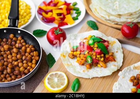 Tacos à la tortilla végétalienne avec pois chiches, poivrons, maïs, tomates, feuilles de basilic et piment vert. Sur le fond sont les ingrédients, les citrons, les pois chiches Banque D'Images