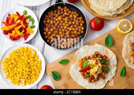 Tacos à la tortilla végétalienne avec pois chiches, poivrons, maïs, tomates, feuilles de basilic et piment vert. Sur le fond sont les ingrédients, les citrons, les pois chiches Banque D'Images