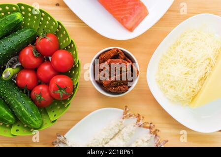 Durée de vie des aliments crus dans des assiettes blanches sur une table en bois. Saumon surgelé sur une assiette à côté de concombres et de tomates, fromage râpé Banque D'Images