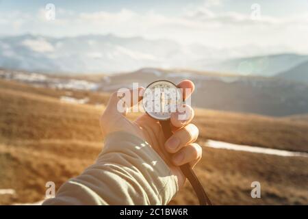 la main d'un homme tient un compas portable sur fond de montagnes et de collines au coucher du soleil. Le concept de voyage et de navigation Banque D'Images