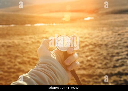 la main d'un homme tient un compas portable sur fond de montagnes et de collines au coucher du soleil. Le concept de voyage et de navigation Banque D'Images