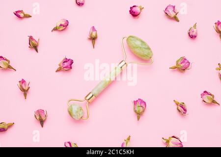 Rouleau de massage pour visage avec deux pierres de jade sur fond rose avec des fleurs de roses séchées autour. Concept de soins de santé. Vue de dessus Banque D'Images