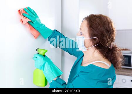 Femme désinfectant les surfaces dans sa maison avec des gants et un masque facial de protection. Coronavirus, concept Covid-19. Banque D'Images