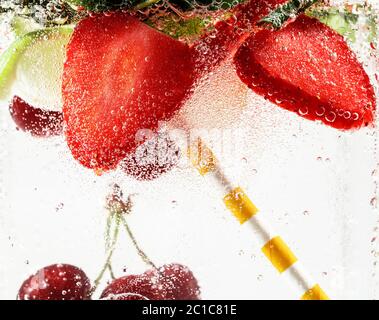 Vue rapprochée de la limonade froide et fraîche avec fraise, cerise, feuilles de menthe et glaçons. Texture de la boisson rafraîchissante de l'été avec des bulles macro sur le verre. Fizing ou flottant jusqu'au sommet de la surface. Banque D'Images