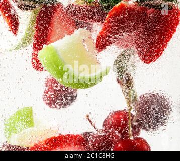 Vue rapprochée de la limonade froide et fraîche avec fraise, cerise, feuilles de menthe et glaçons. Texture de la boisson rafraîchissante de l'été avec des bulles macro sur le verre. Fizing ou flottant jusqu'au sommet de la surface. Banque D'Images