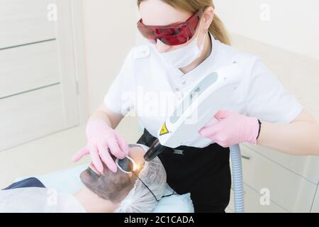 La fille de cosmétique en lunettes de protection fait la procédure de décollement du carbone avec l'aide d'un laser de cosmologie. Écaillage du visage en carbone Banque D'Images