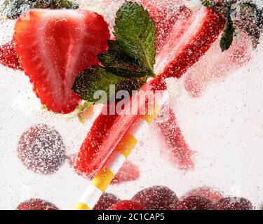 Vue rapprochée de la limonade froide et fraîche avec fraise, cerise, feuilles de menthe et glaçons. Texture de la boisson rafraîchissante de l'été avec des bulles macro sur le verre. Fizing ou flottant jusqu'au sommet de la surface. Banque D'Images