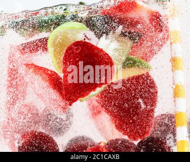Vue rapprochée de la limonade froide et fraîche avec fraise, cerise, feuilles de menthe et glaçons. Texture de la boisson rafraîchissante de l'été avec des bulles macro sur le verre. Fizing ou flottant jusqu'au sommet de la surface. Banque D'Images