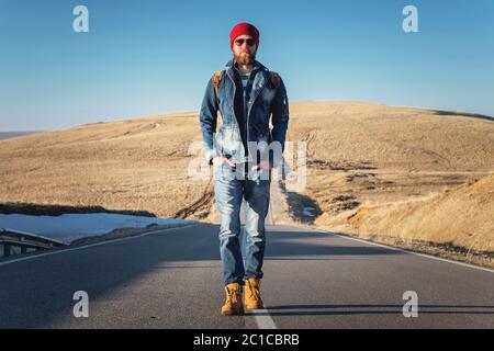 Un élégant boxeur à dos rétro et à dos de soleil fait une promenade sur la route asphaltée par une journée ensoleillée. Le concept de hitc Banque D'Images