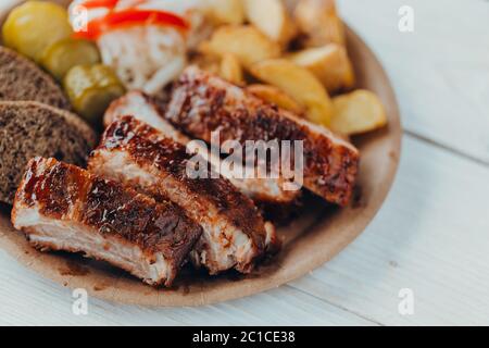 De délicieuses côtes de bœuf avec sauce, des pommes de terre frites, du concombre, du chou et du khlobe dans une assiette en papier sur une table en bois Banque D'Images