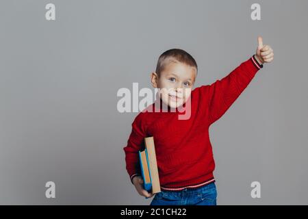 Portrait d'un beau garçon souriant dans un chandail rouge avec des livres en gros plan, sur fond gris Banque D'Images