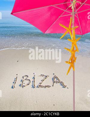 Thème d'été rose parasol jaune étoiles de mer et Ibiza écrit dans le sable Banque D'Images