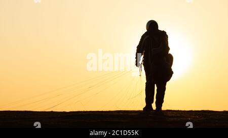 Le parapente se prépare à voler en plein air contre le ciel du coucher du soleil. Parachute dans le sac à dos en plein air Banque D'Images