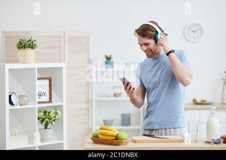 Jeune homme portant un casque souriant en se tenant dans la cuisine et en parlant sur un téléphone portable Banque D'Images
