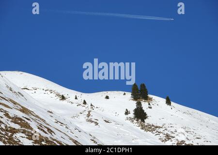 Avion avec pistes de vapeur sur des collines enneigées. Banque D'Images