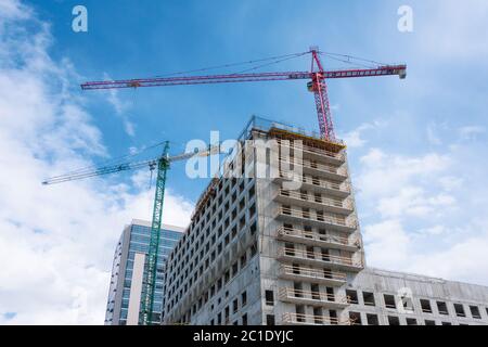 Deux grues érigèrent un bâtiment de plusieurs étages avec des appartements sur fond de ciel bleu avec des nuages Banque D'Images
