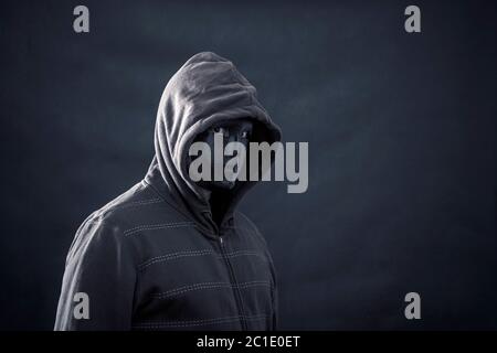 Homme cagoulé avec masque noir dans le noir Banque D'Images