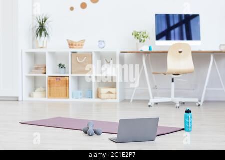 Tapis d'exercice avec haltères et ordinateur portable sur le sol, préparé pour l'entraînement sportif à la maison Banque D'Images