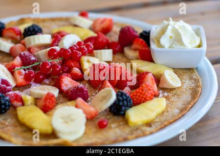 Grande crêpe aux fruits d'été et à la crème fouettée sur une table en bois. Gros plan Banque D'Images