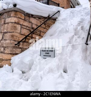 Place neigée dans les escaliers au milieu d'un mur de retenue en pierre avec maison et ciel nuageux Banque D'Images