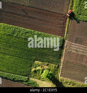 Vue aérienne du drone, une vue d'ensemble de champs agricoles avec une route à travers et un tracteur sur elle au printemps eveni Banque D'Images