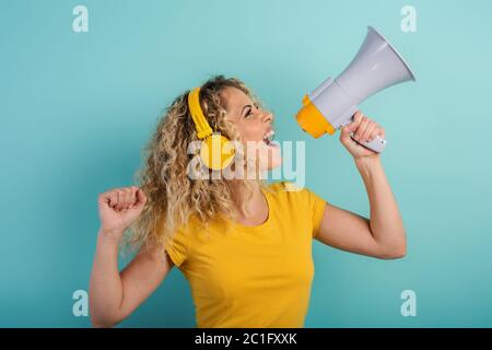 Femme chante avec haut-parleur et écoute de la musique avec casque. Expression joyeuse. Fond cyan Banque D'Images