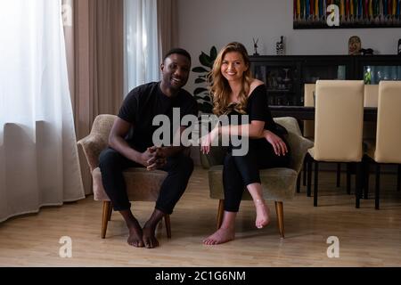 Portrait d'un couple de race mixte souriant assis dans le salon. Regarder la caméra. Banque D'Images