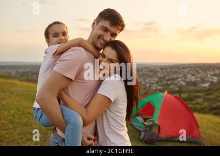 De jeunes parents heureux avec un enfant qui s'embrasse dans leur camp en montagne. Fille avec maman et papa embrassant le voyage de camping Banque D'Images