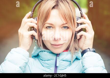 Gros plan Portrait d'une belle jeune femme tenant un casque à l'écoute de musique en plein air dans la forêt. Musique joyeuse Banque D'Images