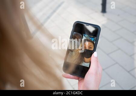 Couple de race mixte masque de visage selfie sur l'écran du téléphone. Vue sur l'épaule. Extérieur. Banque D'Images