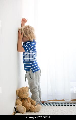 Enfant, tout-petit garçon, puni dans le coin pour avoir fait des faux-grilles à la maison Banque D'Images