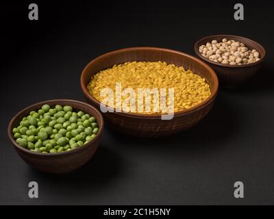 Pois verts biologiques, lentilles jaunes et pois chiches sur fond noir. Banque D'Images