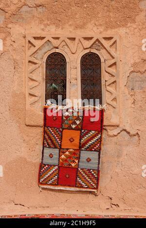 Maroc, Marrakech, tapis berbères marocains colorés typiques suspendus sur un mur en adobe. Banque D'Images