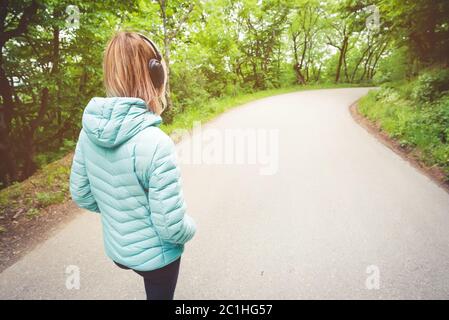 Portrait d'une jolie fille blonde sportive du dos à la veste de course légère, avec casque bluetooth et musique o Banque D'Images