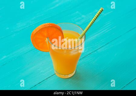 Jus d'orange avec glace et paille dans un verre sur table en bois bleu turquoise, vue du dessus Banque D'Images