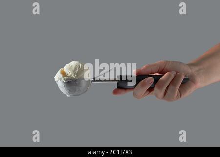 Une boule de glace à la vanille crème blanche dans un metal scoop est titulaire d'une main de femme sur un fond gris. Copier l'espace. Banque D'Images