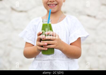 La petite fille boit du jus vert frais en utilisant de la paille à l'extérieur Banque D'Images