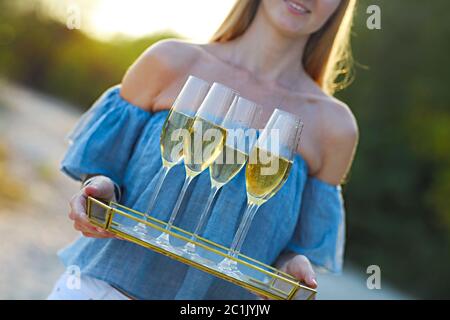 Bonne femme tenant un plateau avec du champagne vin mousseux dans des verres à l'extérieur sur une plage Banque D'Images