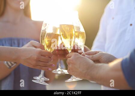 Des amis heureux avec du champagne mousseux dans des verres à l'extérieur sur une plage Banque D'Images