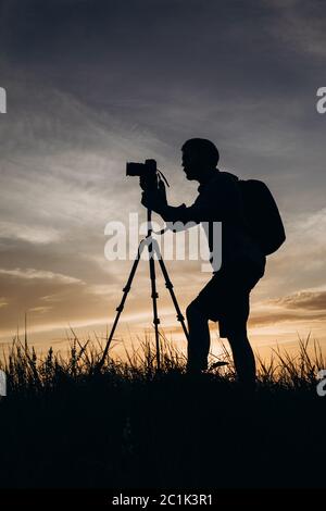 Photographe en silhouette utilisant un trépied pour photographier le coucher du soleil Banque D'Images