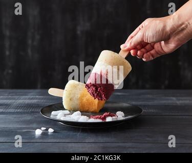 La main d'une femme prend un café fruité crème glacée maison lally dans une assiette noire avec des glaçons sur un fond en bois sombre avec c Banque D'Images