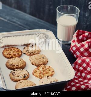 Biscuits d'avoine fait maison sur une plaque de cuisson avec un verre de lait pour le Père Noël sur une table en bois noir. Banque D'Images