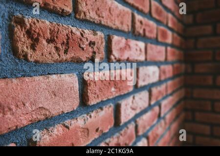 Angle latéral d'un coin de mur en brique rouge. Vue rapprochée du matériau de maçonnerie endommagé fissuré. Décoration intérieure moderne, perspective unique. Style de lissage Banque D'Images