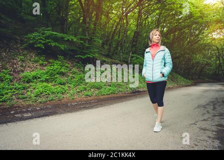 Portrait d'une jolie fille blonde sportive dans une veste de course légère portant un casque bluetooth avec de la musique ou le soun Banque D'Images