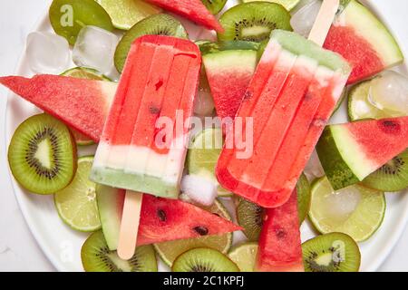 Crème glacée maison rafraîchissante et saine, loci dans une assiette avec des glaçons et des morceaux de kiwi, de citron vert, de pastèque sur un baba blanc Banque D'Images