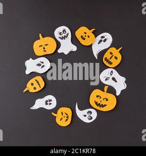 Cadre décoratif de round battant la main flottant esprit fantômes et citrouilles jaune souriant sur un fond de papier noir. Banque D'Images