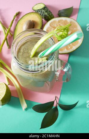 Smoothie vert de légumes biologiques verts avec asperges, céleri, avocat, citron dans un bol en verre sur papier vert rose duotone Banque D'Images