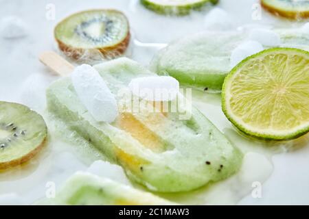 Faire fondre la glace verte sur un bâton avec des morceaux de pêche sur fond gris avec des morceaux de glace, de kiwi, de lime et de kiwi. Été des Banque D'Images