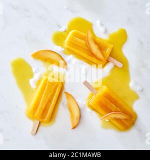 Crème glacée fondue appétissante sur un bâton avec un motif de glaçons et de morceaux de pêche sur un fond de marbre gris Banque D'Images
