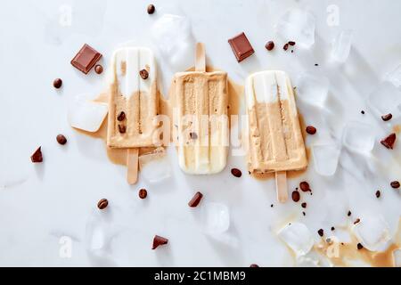 Des pop-suits faits maison au chocolat froid sur un bâton sur fond de glace et de marbre avec un morceau de chocolat et de grains de café, top vie Banque D'Images